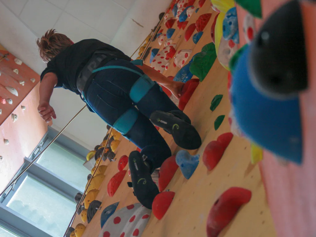 Person klettert quer an einer bunten Kletterwand.